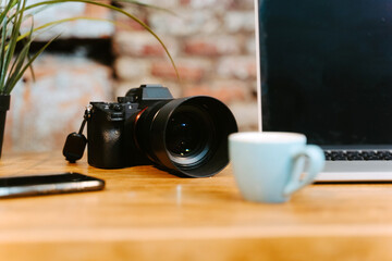 Workplace of freelancer with modern netbook and professional photo camera placed on wooden table with cups of espresso and notepad in cafe