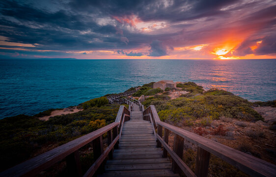Wonderful scenery of endless wooden stairs leading to calm sea under colorful cloudy sky at sunset in Cadiz