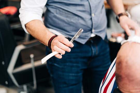Crop unrecognizable male stylist holding straight razor with sharp blade in beauty salon in daytime