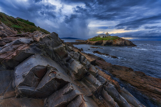 Magnificent dramatic scenery of rough rocky slope of La Picota mountain and small islet with house located in Liencres in Spain in cloudy evening