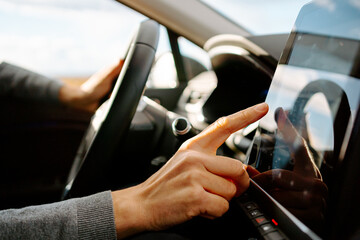 Side view of crop unrecognizable male driver in casual clothes touching screen of GPS navigator while sitting in modern car on sunny day