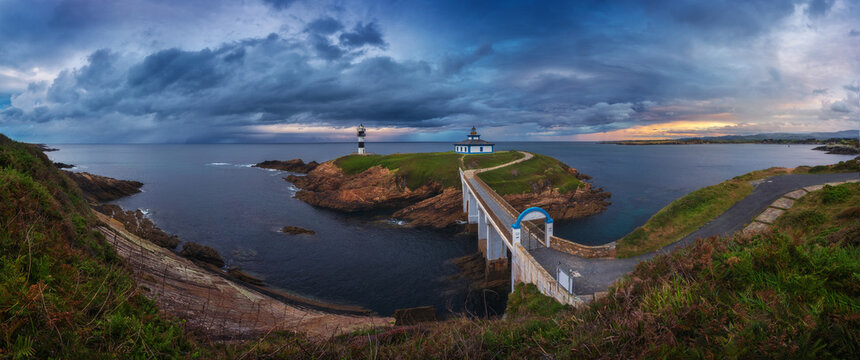 Scenic view of small island with lighthouse called Faro de Cabo Mayor connected with coastline by bridge under dramatic cloudy sky at sunset time in Santander in Spain