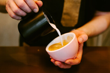 Close-up of a waiter serving milk to a cup of coffee