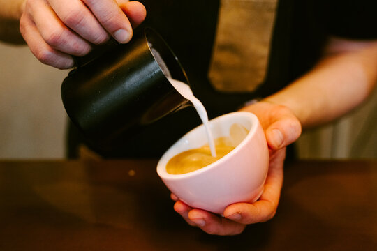 Close-up of a waiter serving milk to a cup of coffee