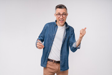 Optimistic mature caucasian man dancing and listening to the music on smart phone isolated in white