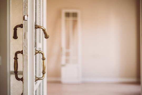 Old fashioned white wooden opened door with ornamental handles in retro style in empty apartment
