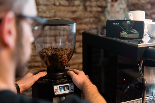 Male barista using electric grinder and grinding coffee beans while working in cafe
