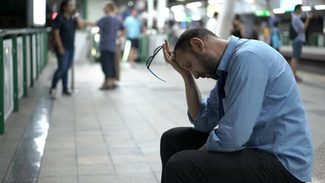 Tired overworked businessman having headache, sitting at train station
