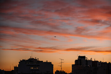 Remote view of helicopter silhouette on background of vivid sundown sky over city in evening