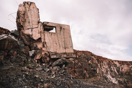 Piece of destroyed cement building on open pit with rough stones under cloudy sky in daylight