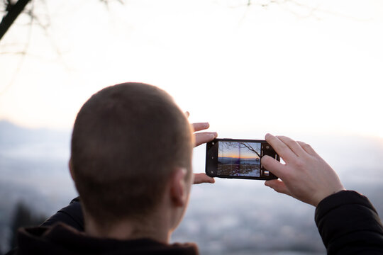 Man taking photos on her smartphone of a sunset in nature.