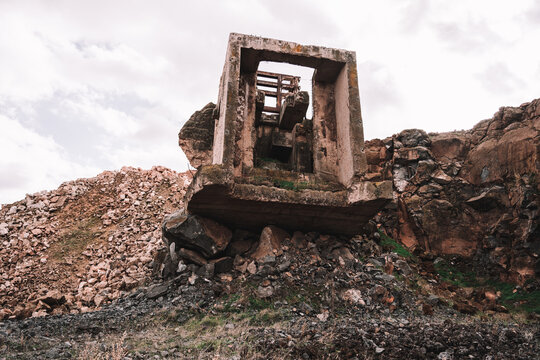 Piece of destroyed cement building on open pit with rough stones under cloudy sky in daylight