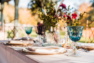 Close-up of served festive table with crystal glasses cutlery napkin on plate near bunch of fresh flowers for wedding