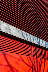 Facing the building with a ventilated facade. Red colored facade with the shadow of a tree. Modern...