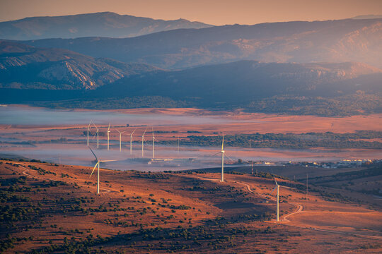 Wind turbines for alternative energy located in valley surrounded by hazy mountain ridge near Cadiz city in Andalusia region of Spain