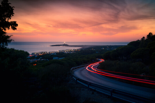 Spectacular scenery of winding road with light trails and coastal city near sea under sunset sky in Cadiz - Powered by Adobe