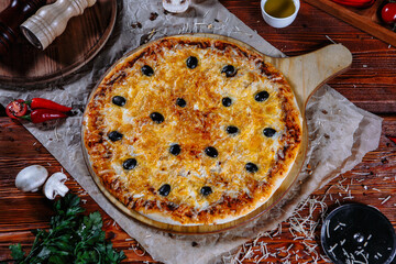 The pizza is on the kitchen table, and the ingredients are scattered around. Cheese pizza with olives