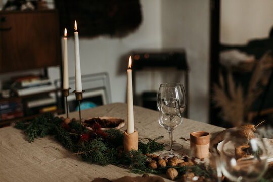 Cozy Xmas interior in natural rustic style with table decorated with burning candles and decorative elements in room with glowing garland