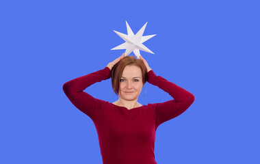 Fototapeta na wymiar A woman in a red dress tries on a paper star on her head. On a blue isolated background.