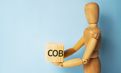 Wooden man holding a wooden cube with acronym COB-COST OF BUSINESS. Business and finances concept.