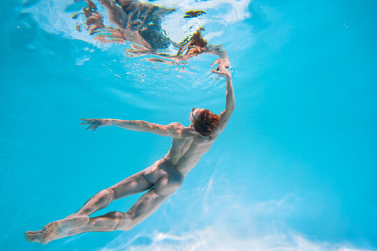 Male Caucasian man swimmer diver dancer swims under water in the sea. Summer tourism, travel journey trip voyage, holiday and vacation. Concertation, art, beauty and freedom concept