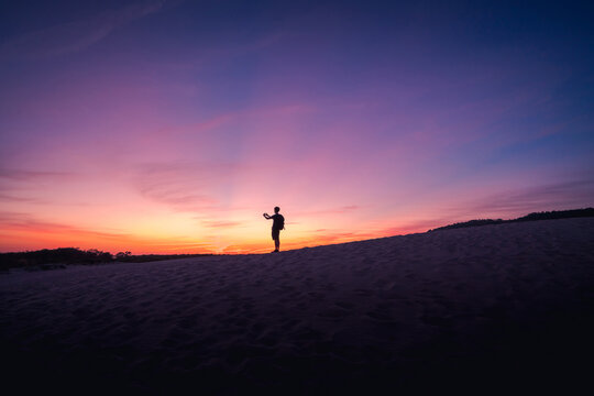 Silhouette of anonymous tourist standing on sandy shore and taking picture of spectacular sundown in Cadiz