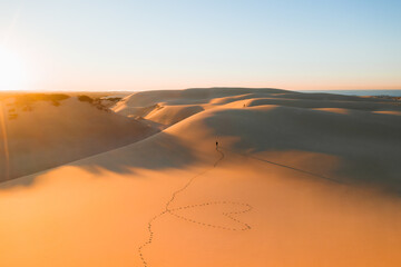 From above distant unrecognizable traveler walking on picturesque sandy dunes near ocean against cloudless sunset sky in Australia