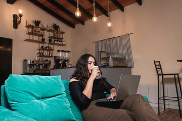 A businesswoman sipping a cup of coffee while working from her notebook in the coffee shop.