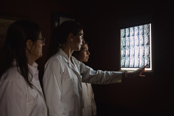 A group of female doctors are looking a x-ray in a dark room with the light off and one is pointing it