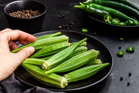Crop unrecognizable person holding ripe okra over table with fresh vegetables on frying pan
