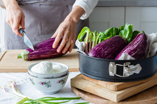 Unrecognizable chef in apron cutting eggplant with knife on cutting board while cooking healthy lunch in kitchen