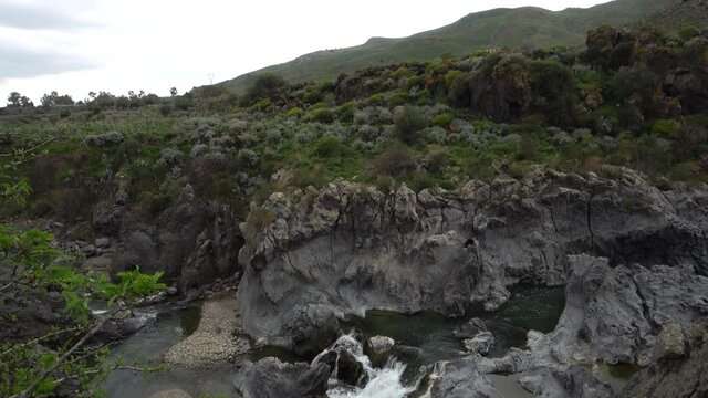 natural landscape of sicilian water stream flowing on volcanic rocks tilt and zoom on a cascade at the exit from a gorge of Simeto River 