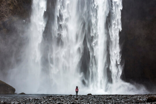 Back view of unrecognizable traveler standing near amazing waterfall in mountains during vacation in Iceland