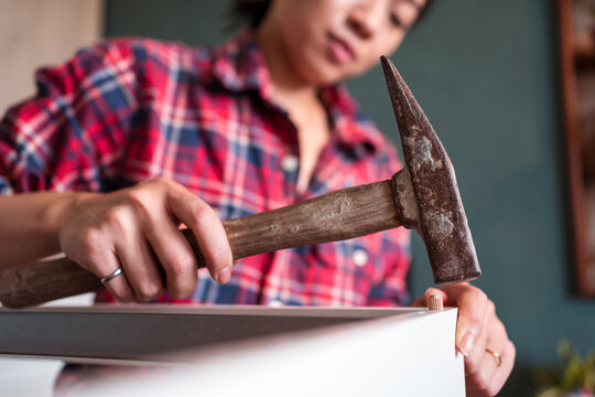 From below focused ethnic female using hammer for nailing wooden dowels while assembling new furniture in apartment