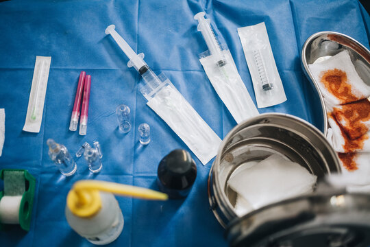 Operating room table with a blue tablecloth with needles, iodine gauze, anesthesia and a metal pot among other tools
