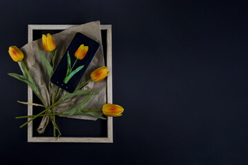 yellow tulips and smartphone in frame on black background