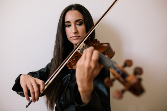 Serious artist playing stringed musical instrument while practicing skills standing against white background