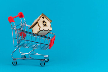 Buying a house or mortgage concept. Model toy house flying with shopping cart on blue background....