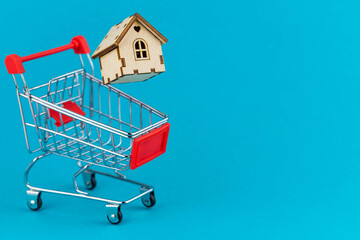 Buying a house or mortgage concept. Model toy house flying with shopping cart on blue background. Housing and Real Estate concept.