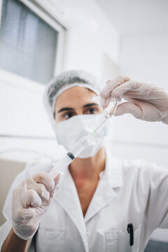 Vertical photo of a doctor with mask, cap and gloves filling a needle with anesthesia in an hospital room