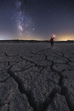 Tourist standing in rocky arid terrain with flashlight under starry sky at night