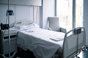 Empty bed with nurse call button near IV stand in light equipped ward in contemporary hospital