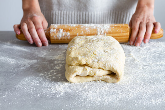 Crop unrecognizable female chef rolling out soft dough using wooden rolling pin with flour during cooking process in house