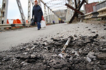 remnants of an exploded ammunition in a crater on the bridge with a walking woman in the background.