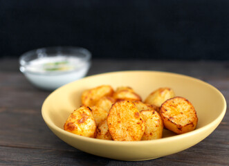 Baked potatoes on yellow plate and white garlic sauce on brown wooden background