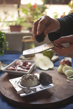 Crop unrecognizable chef sprinkling soft cheese with truffle using grater while cooking at table in house