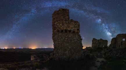 From below picturesque landscape of ancient ruined castle on meadow under Milky Way on starry sky at night