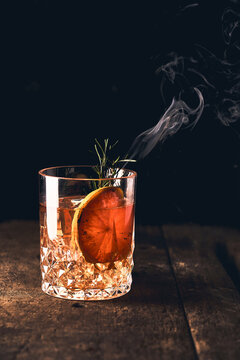 Shiny glass of fresh Negroni cocktail with orange slice garnished with burning sprig of rosemary