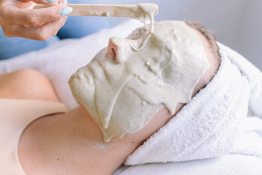Crop unrecognizable cosmetician applying alginate mask on face of anonymous young female customer lying on couch with closed eyes