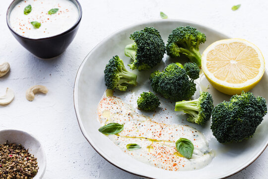 Top view of tasty broccoli with fresh lemon and sauce near bowls with olive oil and spice mix on table
